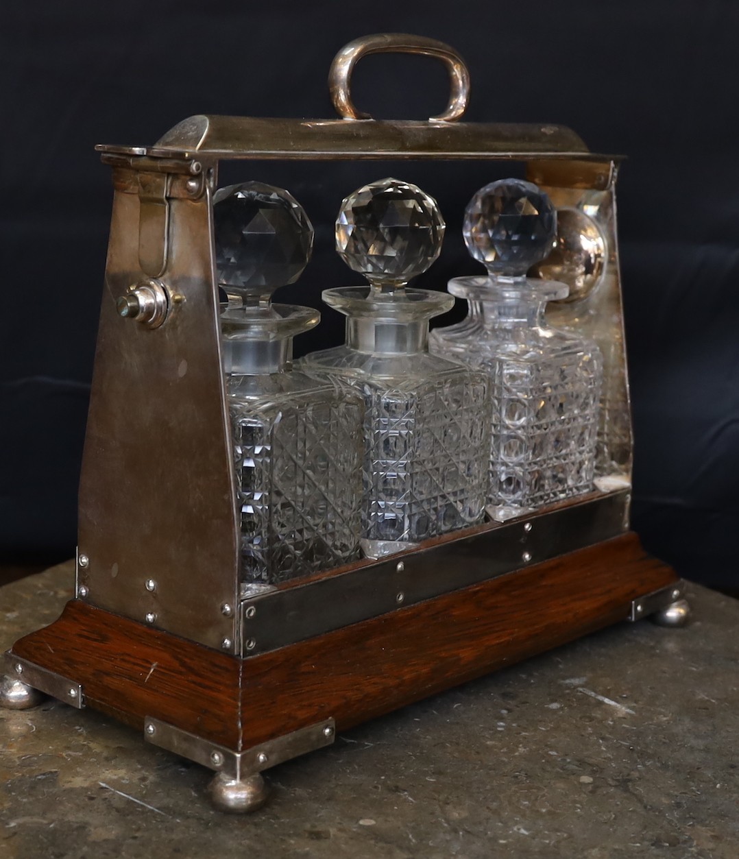 An Edwardian silver plated mounted oak tantalus fitted with three cut glass decanters, width 36cm